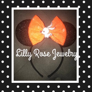 May include: Black and orange sparkly Minnie Mouse ears with a white ghost bow and the text "Lilly Rose Jewelry".