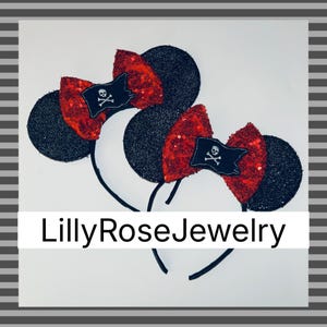 May include: Two black sequined mouse ear headbands with red sequined bows. Each bow features a small black flag with a white skull and crossbones. The text "LillyRoseJewelry" is displayed on a white banner.
