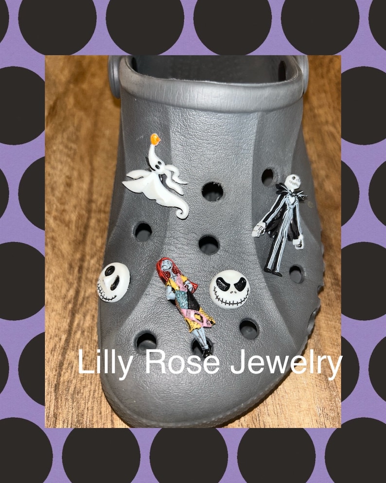 Op de afbeelding: Grijze schoen met verschillende bedels van personages uit Nightmare Before Christmas. De bedels zijn Jack Skellington, Sally, Zero de spookhond en Oogie Boogie. De schoen heeft de tekst "Lilly Rose Jewelry" op de onderkant.