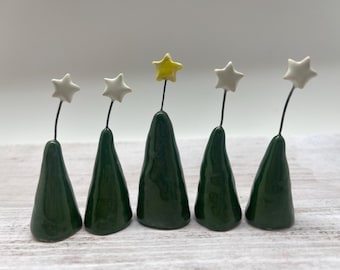 May include: Five small ceramic Christmas trees with star toppers. The trees are green and the stars are white and yellow.