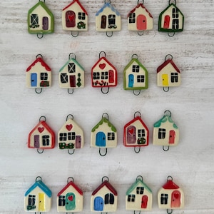 May include: Twenty-four ceramic house charms with various colored doors, windows, and roofs. Each charm has a small loop for hanging.