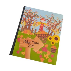 May include: A colorful illustrated cover for a 2024 Miller Maze event guide. The cover features a scarecrow standing in a field with pumpkins, sunflowers, and fall leaves. The text "Miller Maze 2024" is written on a wooden sign.