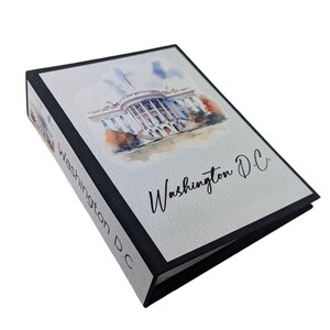 May include: A white three-ring binder with a black spine and edges. The front cover features a watercolor illustration of the White House and the text Washington D.C. in black script. The spine also displays the text Washington D.C. in black.