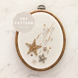 May include: A close-up of a white embroidery hoop with a gold star and shooting stars design. The hoop is on a white marble surface. The text "PDF PATTERN & GUIDE" is on a beige circle.
