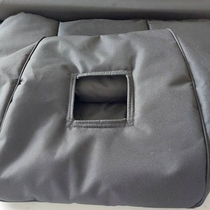 Könnte beinhalten: Eine schwarze, rechteckige Tasche mit einer quadratischen Öffnung in der Mitte. Die Tasche besteht aus einem glatten, matten Stoff und hat ein gepolstertes Aussehen. Die Kanten sind sauber mit einem kontrastierenden Besatz genäht.