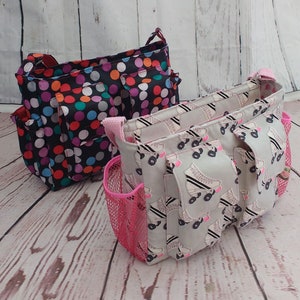 Può includere: Due borse in tessuto con manici. Una borsa è nera con pois colorati e l'altra è grigia con un motivo di pattini a rotelle bianchi. Entrambe le borse hanno più tasche.