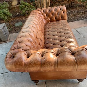 May include: A brown leather tufted sofa with a distressed finish. The sofa has a classic design with rolled arms and a button-tufted back.