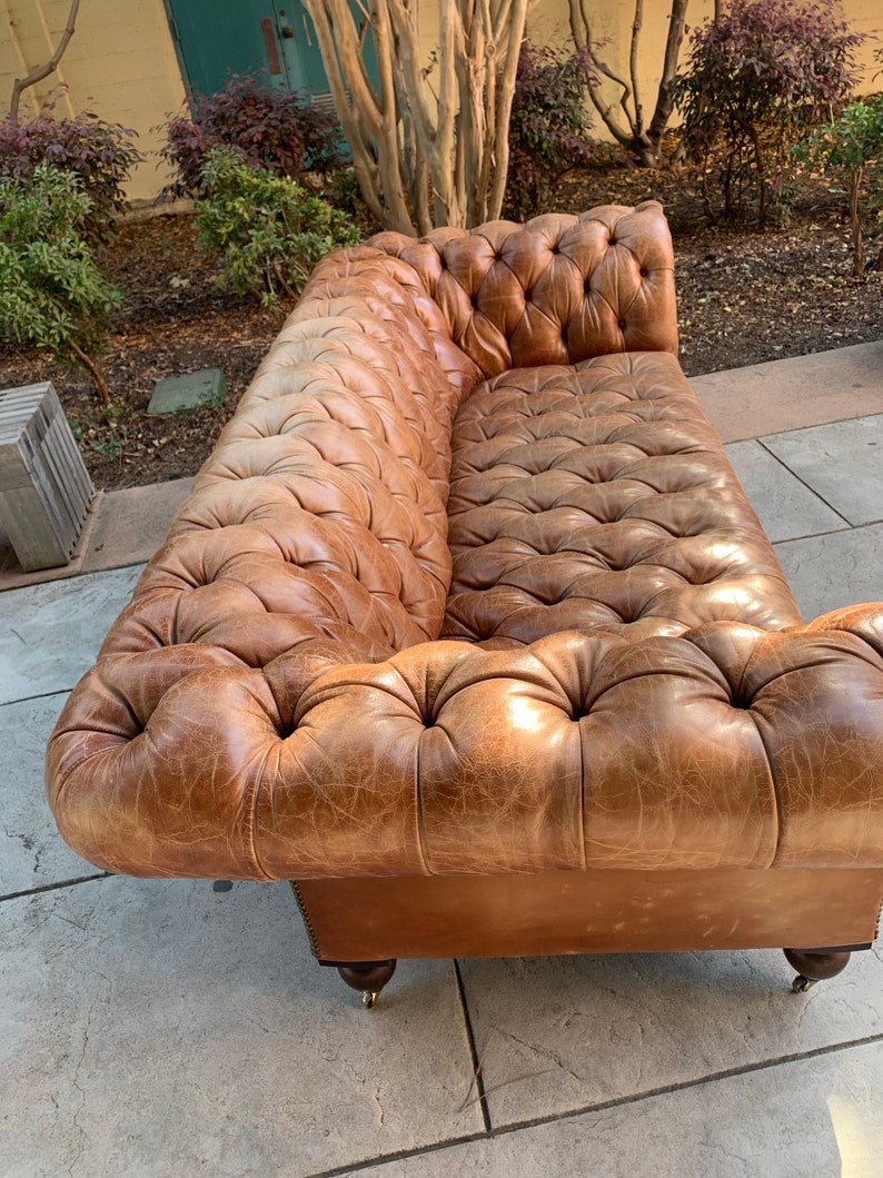 May include: A brown leather tufted sofa with a distressed finish. The sofa has a classic design with rolled arms and a button-tufted back.