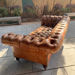 May include: A brown leather tufted sofa with a distressed finish. The sofa has a rolled back and arms and sits on four wooden legs with casters.