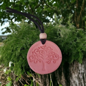 May include: A pink ceramic pendant with a tree of life design. The pendant is on a black cord with a wooden bead.