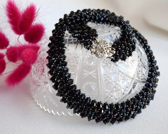 May include: A black beaded necklace with a silver clasp. The necklace is made of small, faceted beads that are arranged in a geometric pattern.