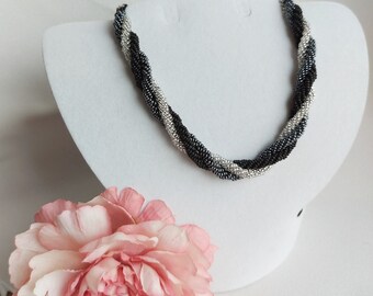 May include: A black, silver, and gray beaded necklace with a twisted design. The necklace is displayed on a white mannequin bust.