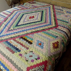May include: A large, colourful quilt made of patchwork fabric. The quilt is made up of many different colours and patterns, including pink, blue, green, yellow, and red. The quilt is made in a hexagonal pattern, with each hexagon being a different colour and pattern. The quilt is a beautiful example of handmade craftsmanship.