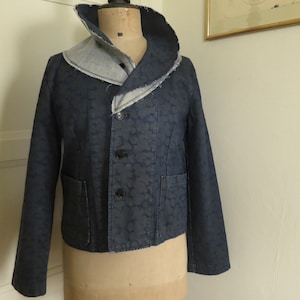 Peut inclure: Une veste en jean bleu foncé avec un grand col contrastant en jean bleu clair. La veste a une fermeture à boutons et deux poches.