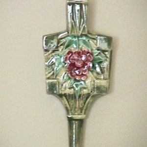 May include: A ceramic wall hanging in the shape of a flower pot with a green and brown bamboo design and a red flower. The flower pot has a long, narrow spout at the bottom.