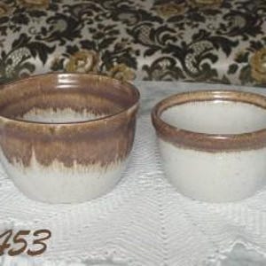 May include: Two ceramic plant pots, one larger than the other. Both are white with a brown glaze, creating a mottled effect. The larger pot is wider and rounder, while the smaller pot is more cylindrical. #1453