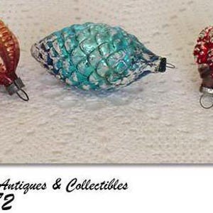 May include: Three vintage glass Christmas ornaments. One is red with white accents, one is blue with silver accents, and one is red and white with a ribbed design.
