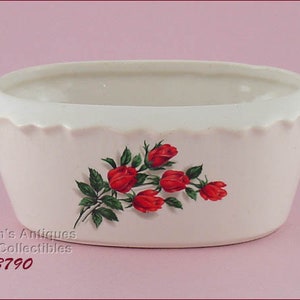 May include: A cream-colored, oval-shaped ceramic planter with a scalloped rim. The planter features a floral design of red roses and green leaves. The text "Lin's Antiques & Collectibles #3790" is printed on the side.