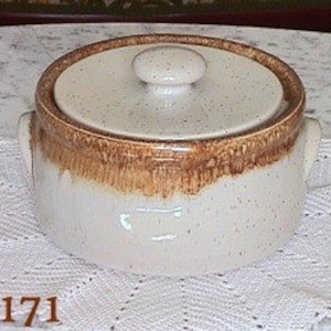 May include: A white ceramic casserole dish with brown speckled glaze and two handles. The lid has a knob and a white speckled glaze.