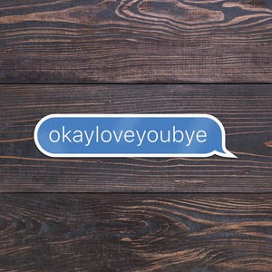 May include: A blue text bubble with the words "okayloveyoubye" in white text, set against a dark brown wooden background. The wood grain is visible, adding texture to the image. The text bubble is a modern design element.