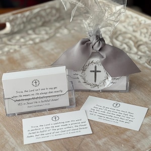 May include: A set of white cards with religious quotes, packaged in a clear plastic holder and wrapped with a gray ribbon. The cards feature a cross and floral design. The text on the cards includes Bible verses.