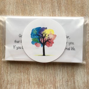 May include: A round sticker featuring a watercolor tree with a rainbow-colored canopy and a black trunk. The sticker is packaged with a white card that has text on it. The sticker is in a clear plastic sleeve.