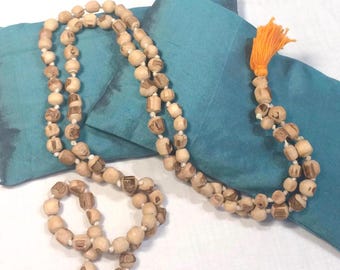 May include: A wooden mala bead necklace with a tassel. The beads are light brown and have a pattern on them. The necklace is lying on a blue fabric background.