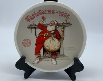 May include: A decorative plate featuring a depiction of Santa Claus in a red suit, holding a sack, and reaching for a decoration above a fireplace. The plate is inscribed with "Christmas * 1995" in red lettering.
