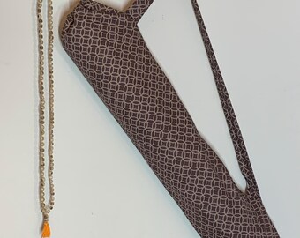 May include: A long, cylindrical fabric bag with a brown and white geometric circle pattern and a shoulder strap, hanging alongside a long string of small, light-colored wooden beads that features a single bright orange tassel at the bottom end.
