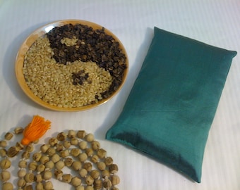 May include: A teal fabric pillow, a bowl filled with brown and black rice, and a wooden beaded necklace with an orange tassel.