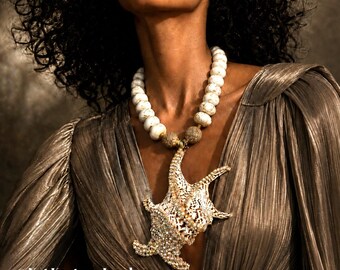 May include: A necklace featuring a large, textured seashell pendant adorned with small crystals, suspended from a strand of round, white, speckled beads. The text "Kat Kouture Jewelry ~ 08.12.2026" and "AI Model Image" is visible at the bottom.
