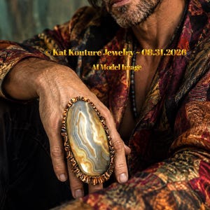 May include: A large oval ring featuring a banded agate stone with swirling cream, tan, and grey patterns, set in a textured copper-toned metal frame. The text Kat Kouture Jewelry - 08.31.2026 and AI Model Image is visible across the center of the image.
