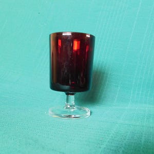 May include: A clear glass stemmed shot glass with a dark red base.