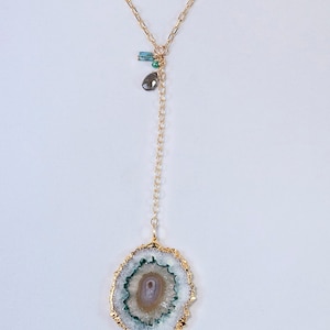 May include: A gold-colored chain necklace with a pendant featuring a white, green, and tan geode slice with gold edging. The necklace also has small blue and green gemstone accents.