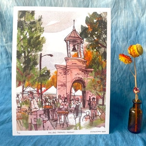 May include: A watercolor painting of the Ballard Farmers Market in Seattle, Washington. The painting depicts a brick archway with a bell tower and people shopping at the market. The text "Ballard Farmers Market" is printed below the image.
