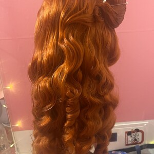 May include: A long, vibrant copper-red wig styled with voluminous, cascading curls that fall down the back. The hair is gathered at the crown in a partial updo, secured with two thin, silver-toned hairpins featuring small, round white decorative beads.