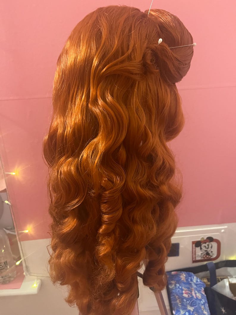 May include: A long, vibrant copper-red wig styled with voluminous, cascading curls that fall down the back. The hair is gathered at the crown in a partial updo, secured with two thin, silver-toned hairpins featuring small, round white decorative beads.