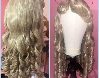 May include: A blonde wig with long, curled hair styled in a vintage updo. The wig is on a mannequin head and is ready to be styled.