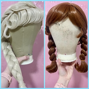 May include: Two synthetic wigs displayed on mannequin heads. The left wig is platinum blonde, styled in a side-swept fringe with a long, thick side braid. The right wig is auburn brown, styled with a center part and two thick, braided pigtails.