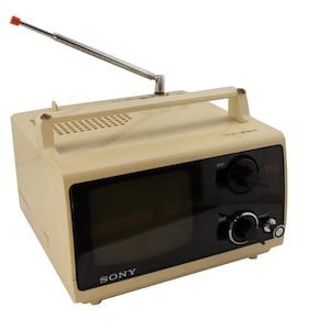 May include: A vintage cream-colored Sony TV-6100 portable television with a black screen and a silver telescopic antenna. The television has a black control panel with knobs and a black speaker grille.