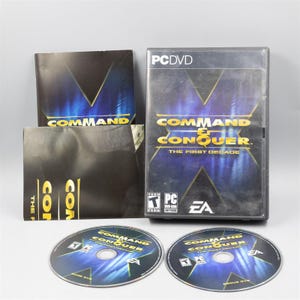 May include: A PC DVD game set, featuring the game "Command & Conquer: The First Decade." The set includes a clear plastic case, two game discs, and several printed inserts. The game's title is in gold lettering against a dark blue and black background.