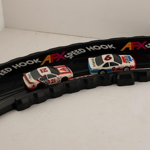 May include: Two miniature race cars on a black track. One car is white with red and orange accents, the number 21, and the Citgo logo. The other car is white with blue and red accents, and the number 6 and 9.