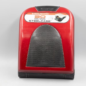 May include: A red Atlantic 30 CD/DVD Steelcase storage unit with a black mesh front panel. The top label features the brand name, capacity, and a graphic illustration of the internal disc storage mechanism. The base is black plastic.