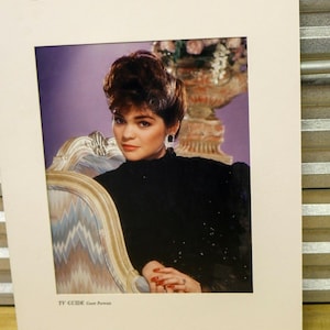 May include: A portrait of a woman in a black dress, seated in an ornate chair. Her hair is styled up, and she wears earrings. The image is from a TV Guide cover, with the text "TV GUIDE Cover Portrait" at the bottom.