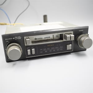 May include: A vintage Clarion 6100R car stereo with a silver faceplate and black trim. Features include tuning and balance knobs, station presets, and AM/FM radio. The stereo has a cassette player and various buttons.