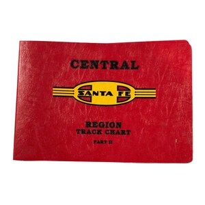 May include: A red rectangular booklet with a textured cover featuring the black text CENTRAL, a yellow oval logo with black horizontal lines and the text SANTA FE, and the black text REGION TRACK CHART PART II printed on the front cover.