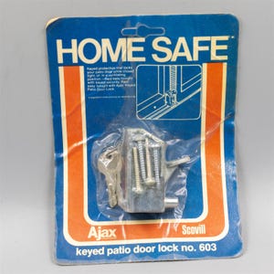 May include: A silver metal keyed patio door lock in original blue and orange packaging labeled HOME SAFE and Ajax Scovill. The package includes a metal lock mechanism, a key, and mounting screws, with a diagram showing installation on a door.