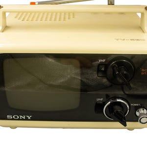 May include: A vintage cream-colored Sony portable television with a black screen and control panel. Features include VHF and UHF dials, a power button, and a handle. The words "SOLID STATE" are visible.