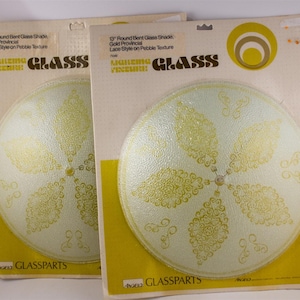 May include: Two 13-inch round bent glass shades with a gold provincial lace style on a pebble texture. The shades are packaged on a yellow and off-white cardboard backing. The packaging includes the text "LIGHTING FIXTURE GLASS".