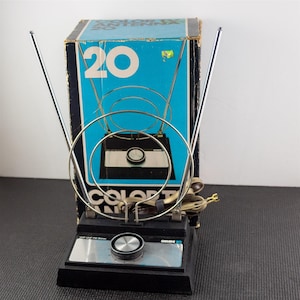 May include: Vintage Gemini 20 color TV antenna with a black base, silver dial, and adjustable chrome antennas. The box behind it is blue and white with the number 20 and the words "Color TV Antenna".